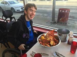 Young man in wheel chair sitting at table with a bowl of seafood