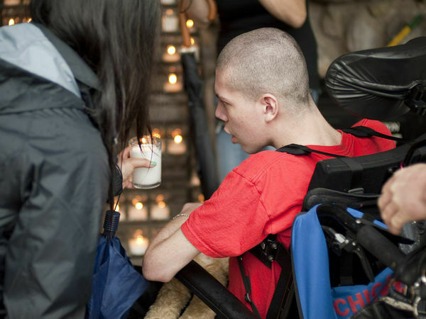 Young man sitting in a wheel chair lighting a candle at the grotto