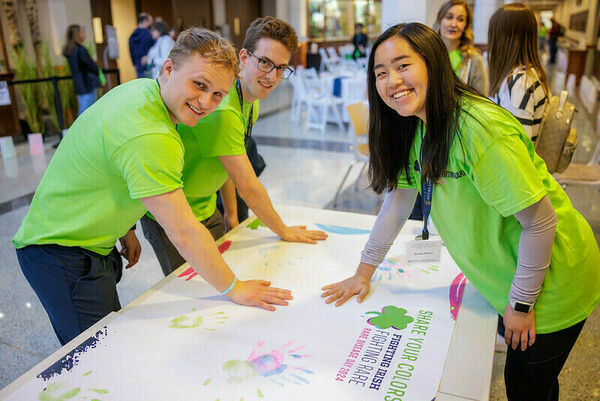 Three students wearing lime green t-shirts press their hands on a banner to create colorful handprints on Rare Disease Day 2024.